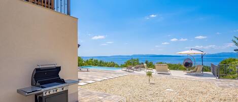 A patio with a grill, seating, and a pool overlooking a scenic view.