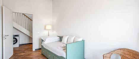 Un dormitorio con cama, una silla, lavadora y una escalera.