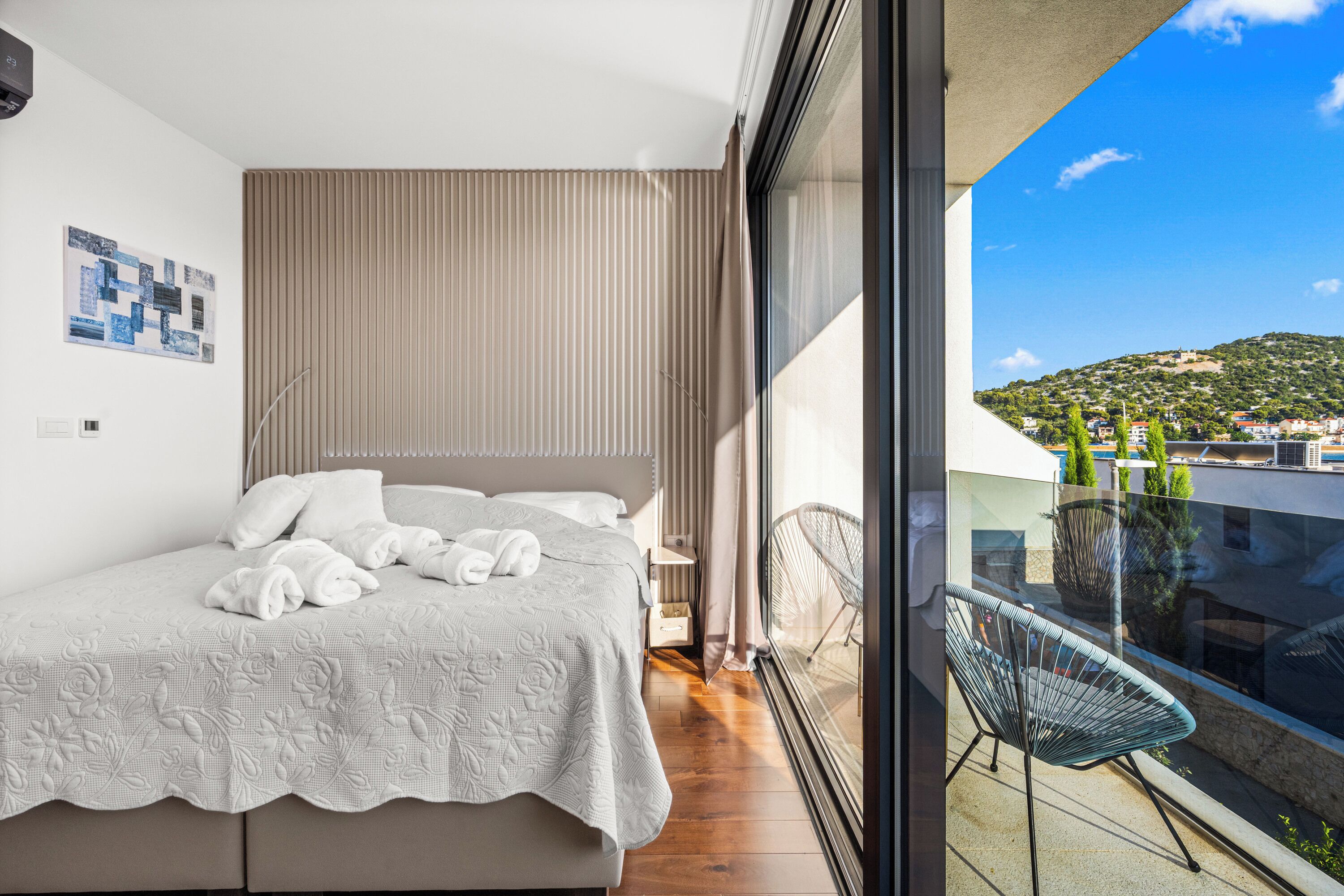Ein Schlafzimmer mit Bett, einem Fenster mit Blick auf eine Hügellandschaft und einem Balkon mit einem Stuhl.