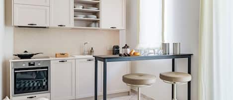 A modern kitchen with white cabinetry, a built-in oven, and a dining area with stools.