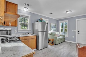 A modern kitchen with a stainless steel refrigerator, a microwave, and a stove. There is a wooden cabinet above the stove and a window with a view of trees.