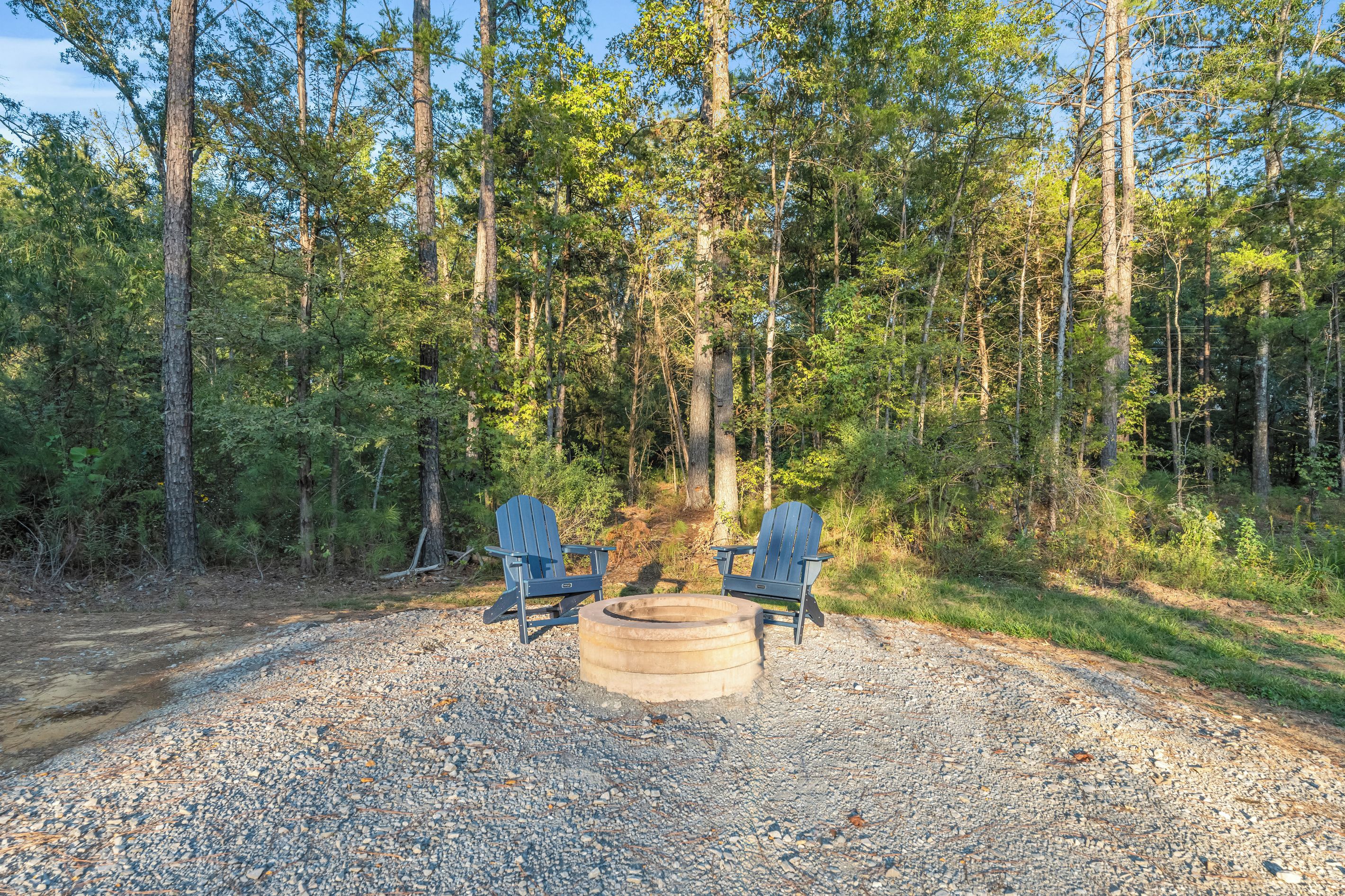 Ein Waldcampingplatz mit zwei Adirondack-Stühlen und einer Feuerstelle.
