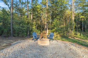 En campingplats i skogen med två Adirondack-stolar och en eldstad.