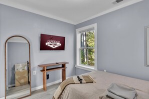 A bedroom with a bed, a TV mounted on the wall, a window with a view of trees, and a mirror.