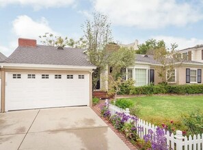 Een woonhuis met een garage, een gazon en een witte picket fence.