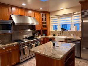 A modern kitchen with granite countertops, stainless steel appliances, wooden cabinets, and a window with blinds. - Elegant, peaceful LA home, 5 min from UCLA (Los Angeles)