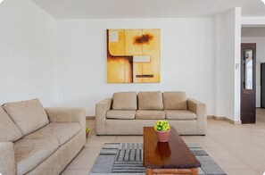 A living room with two sofas, a coffee table with a flower vase, and a large abstract painting on the wall. - Casa Blanca: 4-unit building with rooftop lounge, minutes from 5 Avenida (Playa del Carmen)