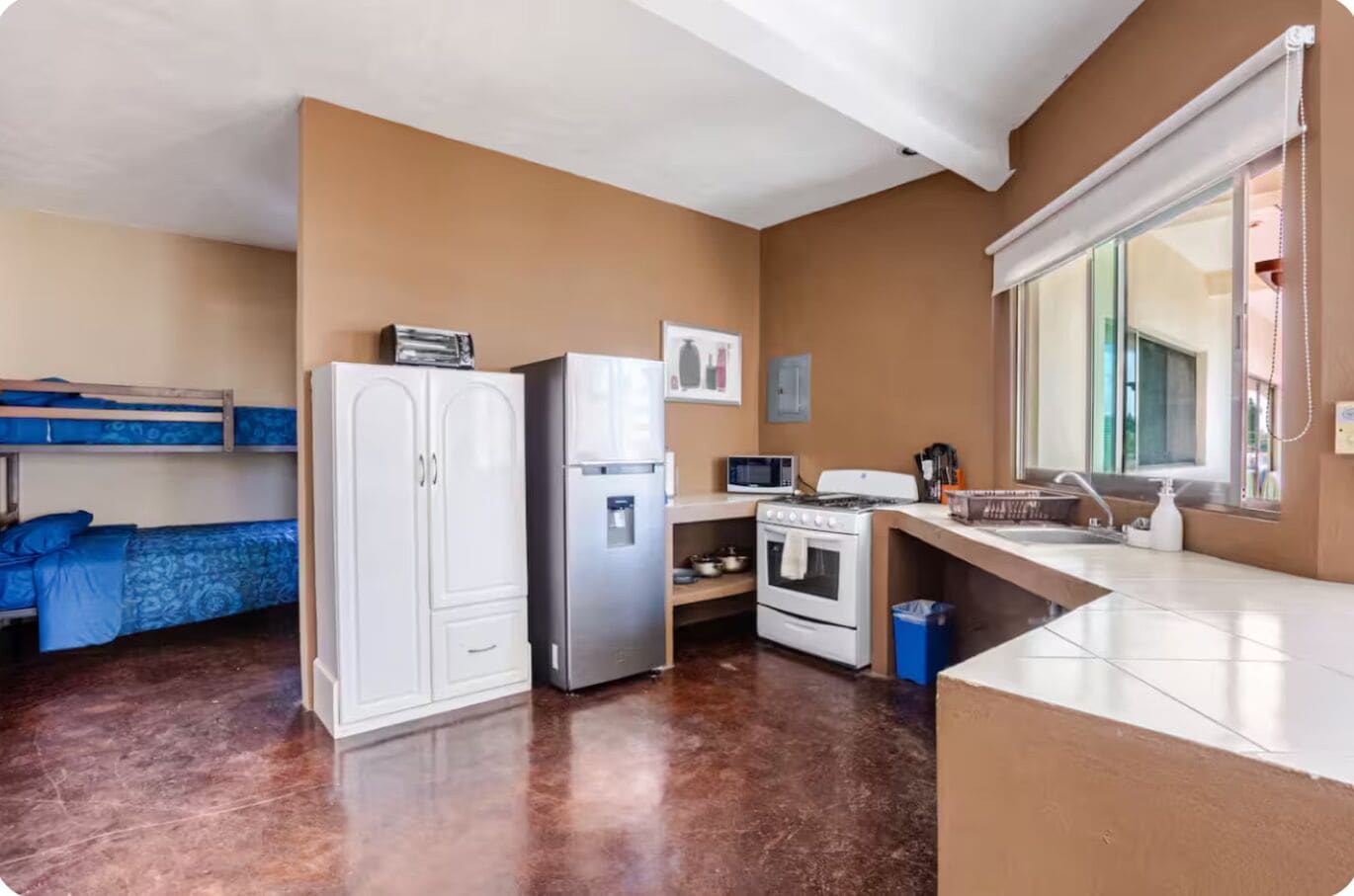 Een kleine kamer met stapelbedden, een kitchenette en een raam.