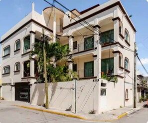 A multi-story residential building with balconies, a gated entrance, and a clear sky. - Casa Blanca: 4-unit building with rooftop lounge, minutes from 5 Avenida (Playa del Carmen)