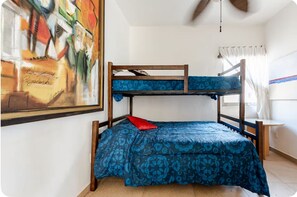 A bunk bed with a patterned bedspread, a painting on the wall, and a window with curtains. - Casa Blanca: 4-unit building with rooftop lounge, minutes from 5 Avenida (Playa del Carmen)