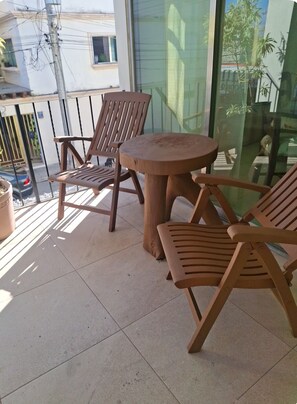 Ein Balkon mit zwei Holzstühlen, einem runden Tisch, einer Glastür und Blick auf ein Gebäude und Bäume.