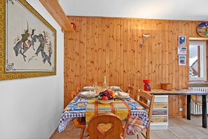 Uma área de refeições com parede revestida de madeira, uma mesa posta para quatro pessoas e um quadro sobre a mesa.