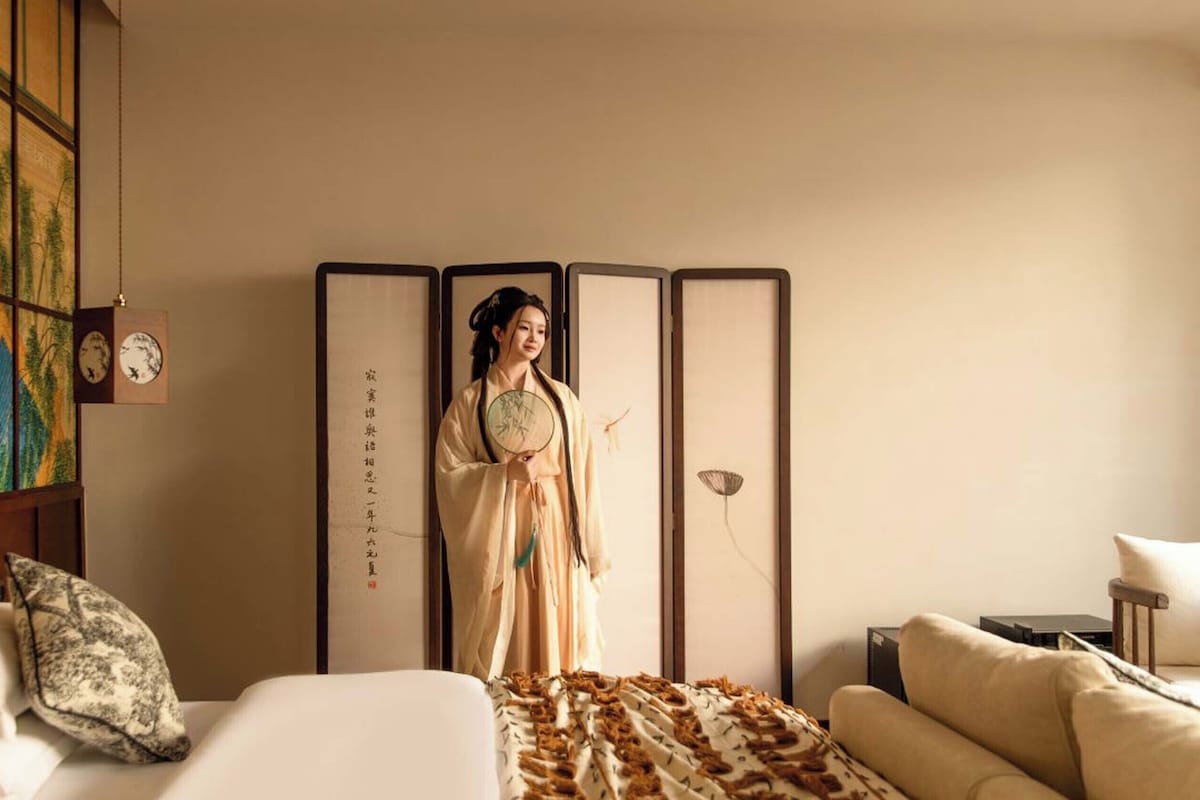 A traditional room with a bed, a sofa, a decorative screen, and a wall with a clock and artwork.