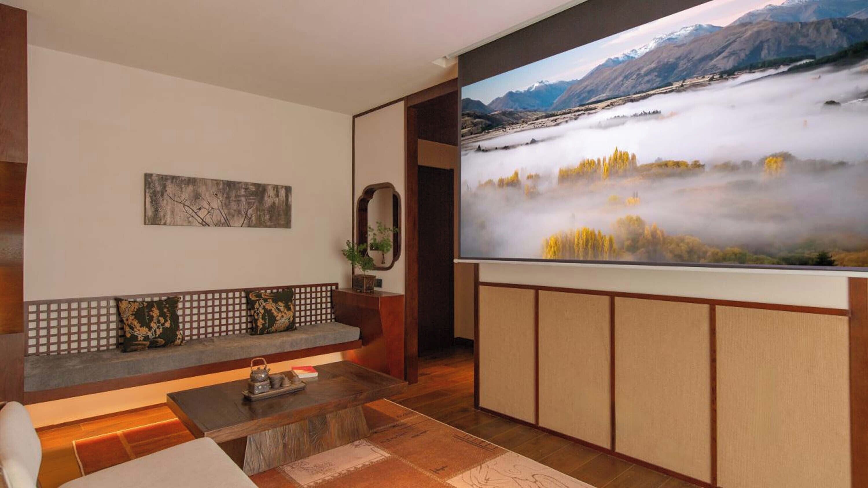 Un soggiorno con una grande TV a schermo piatto, un divano con cuscini, un tavolino da caffè con una teiera e un quadro appeso al muro.