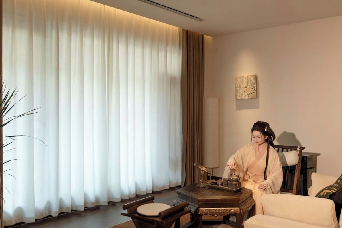 A room with a large window, a sofa, a wooden side table, and a lamp.