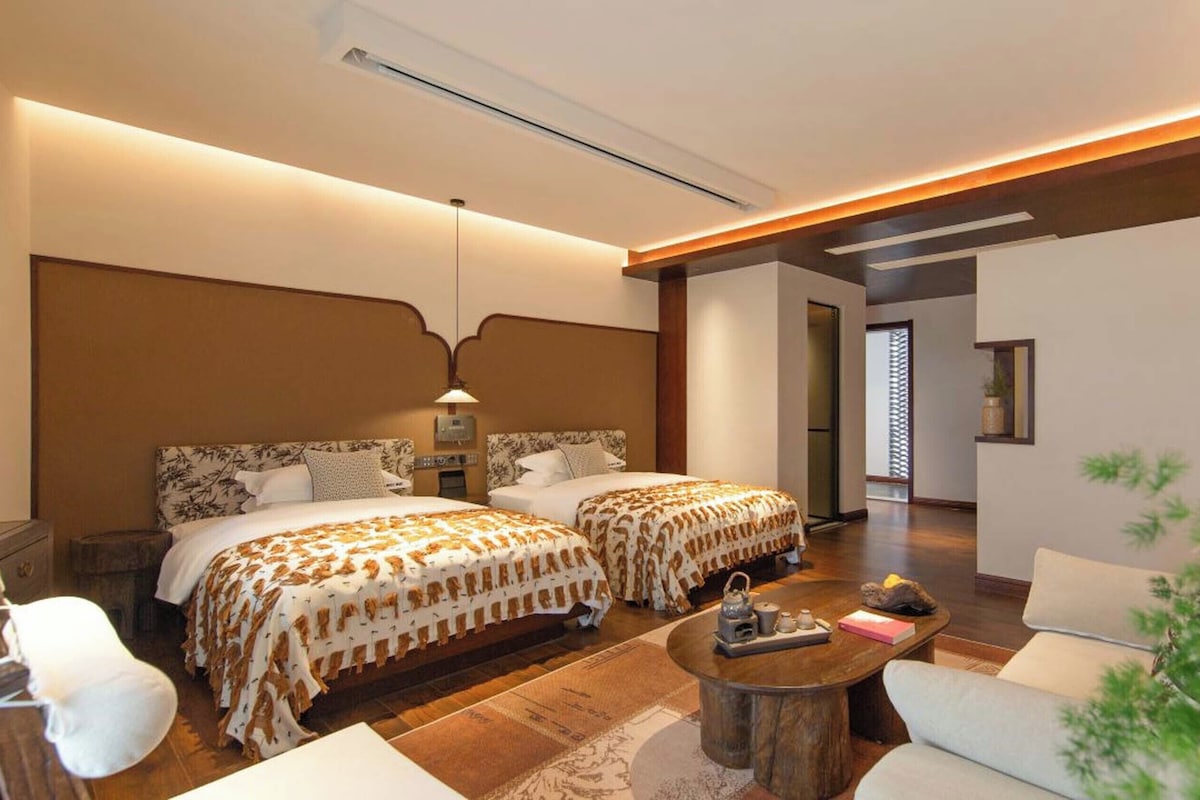 A hotel room with two beds, a sitting area with a coffee table, and a view of the outside.