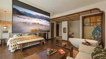 A spacious room with a large bed, a sitting area with a sofa, a coffee table, and a large painting of a mountainous landscape.