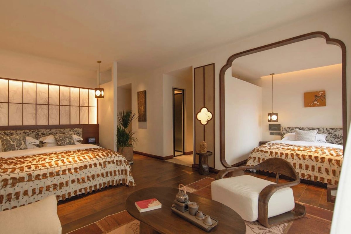 A hotel room with two beds, a large mirror, a coffee table, and a small side table.