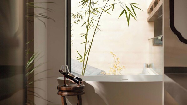 Une pièce avec une grande fenêtre, une plante en bambou et un verre à vin posé sur une petite table en bois.