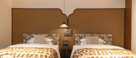 Une chambre d’hôtel avec deux lits, chacun doté d’une tête de lit décorée, d’une table de chevet et d’un panneau de commande fixé au mur.