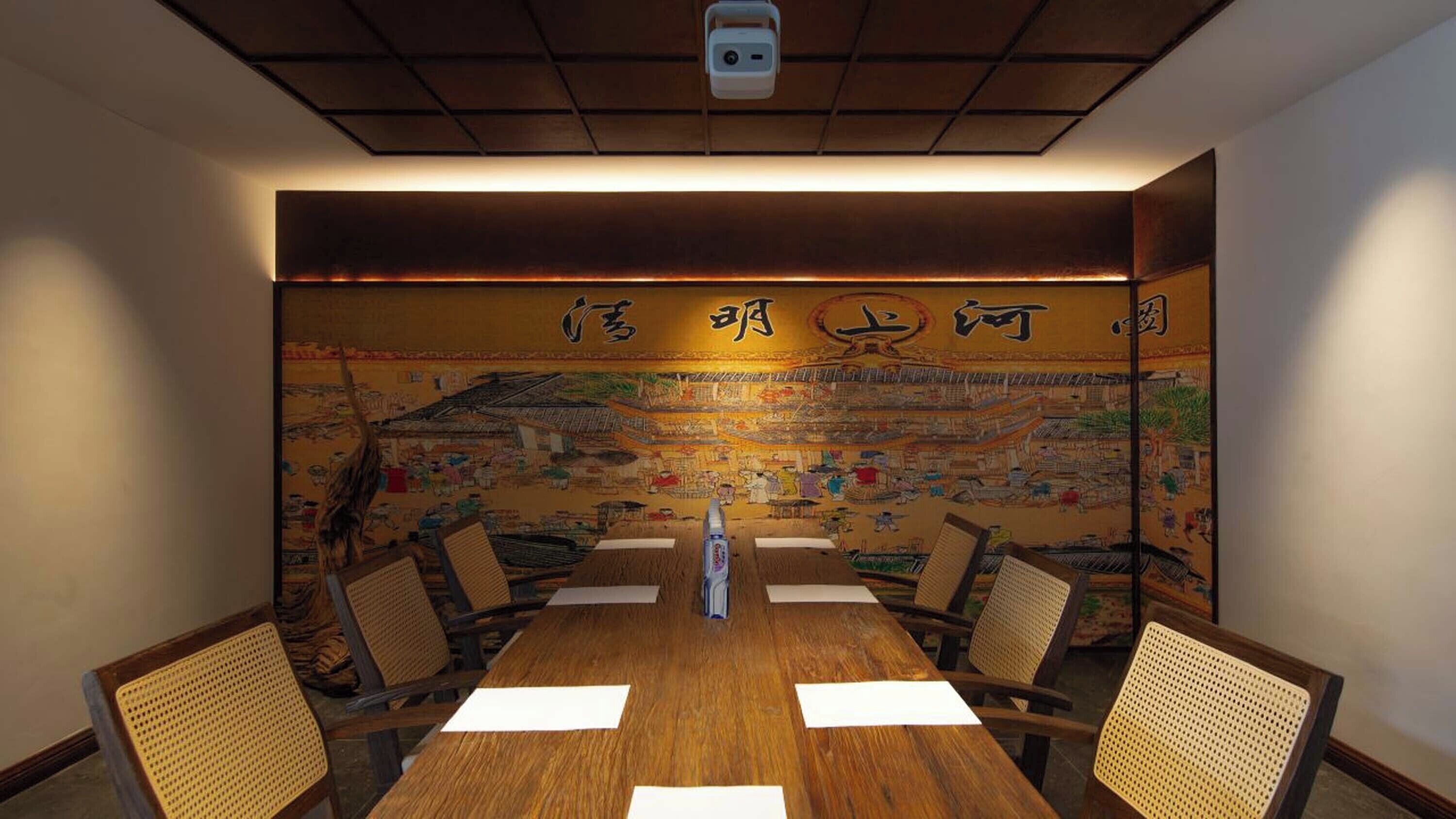 Una sala conferenze con un murale tradizionale cinese sulla parete, un tavolo in legno e sedie in vimini.