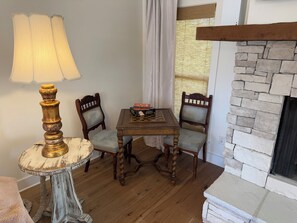 Una habitación con una mesa de madera, dos sillas, una lámpara y una chimenea de piedra.