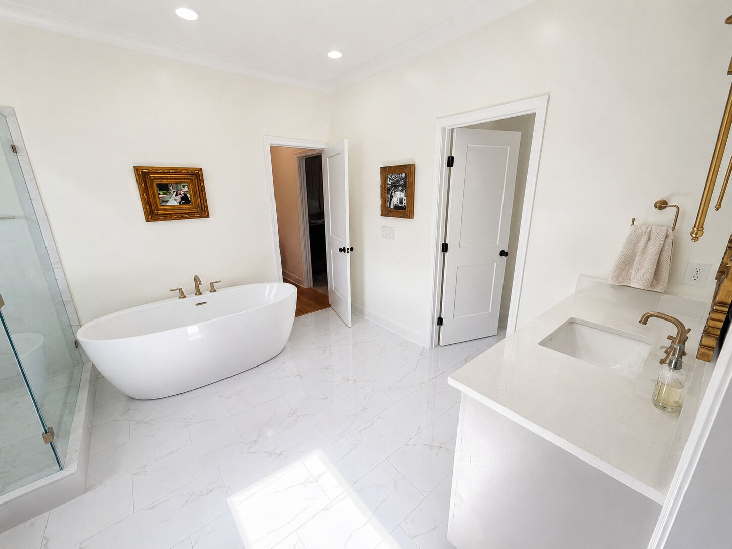 Une salle de bain moderne avec une baignoire sur pieds, un lavabo doté d’un robinet doré et deux portes donnant sur d’autres pièces.