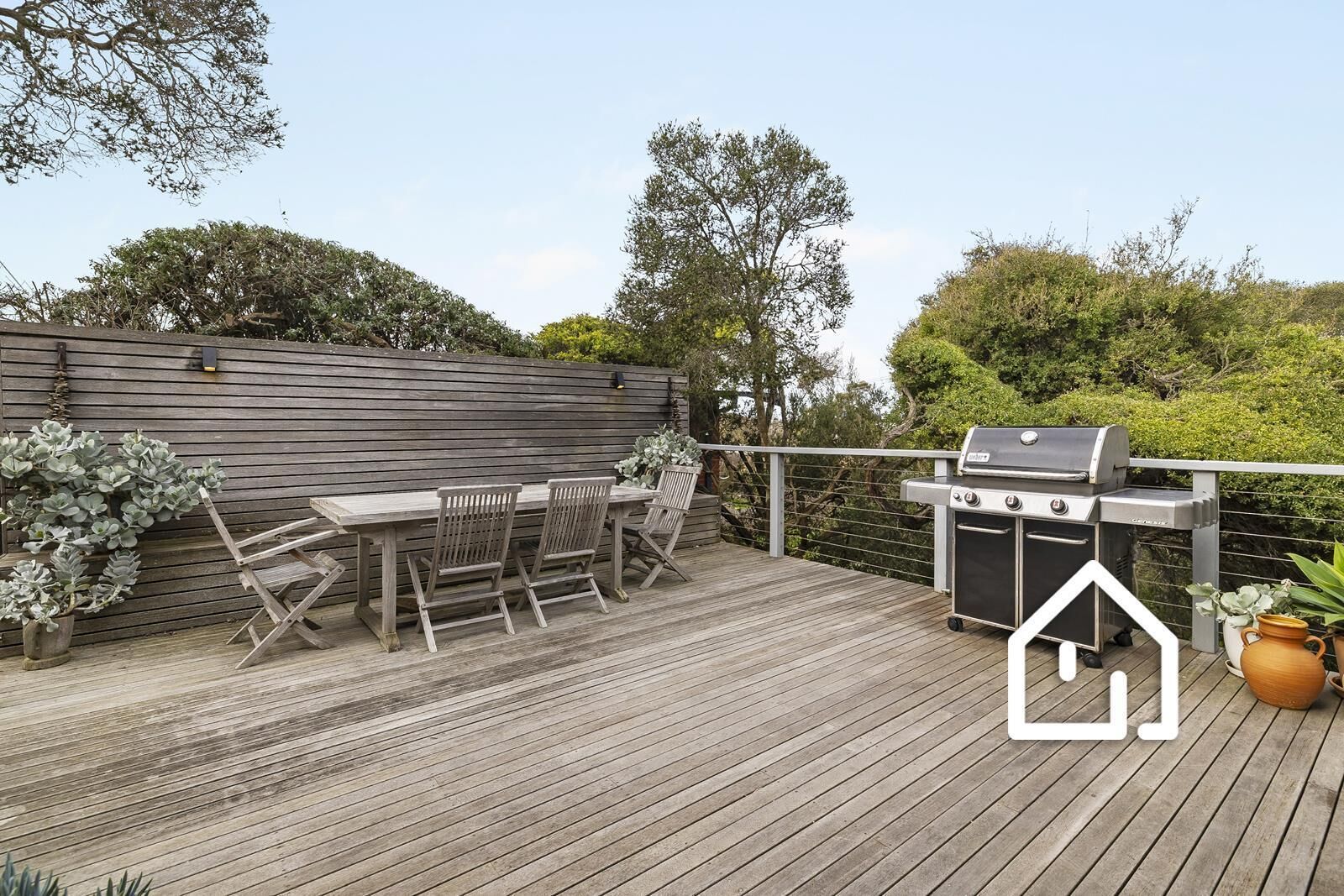 An outdoor deck with a grill, wooden table, and chairs.