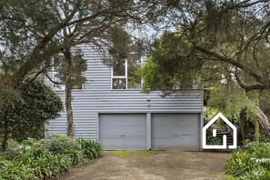A two-story house with a garage door, surrounded by trees and plants. - Ocean Whispers *1 NIGHT FREE* Blairgowrie Back Beach Retreat (Blairgowrie)
