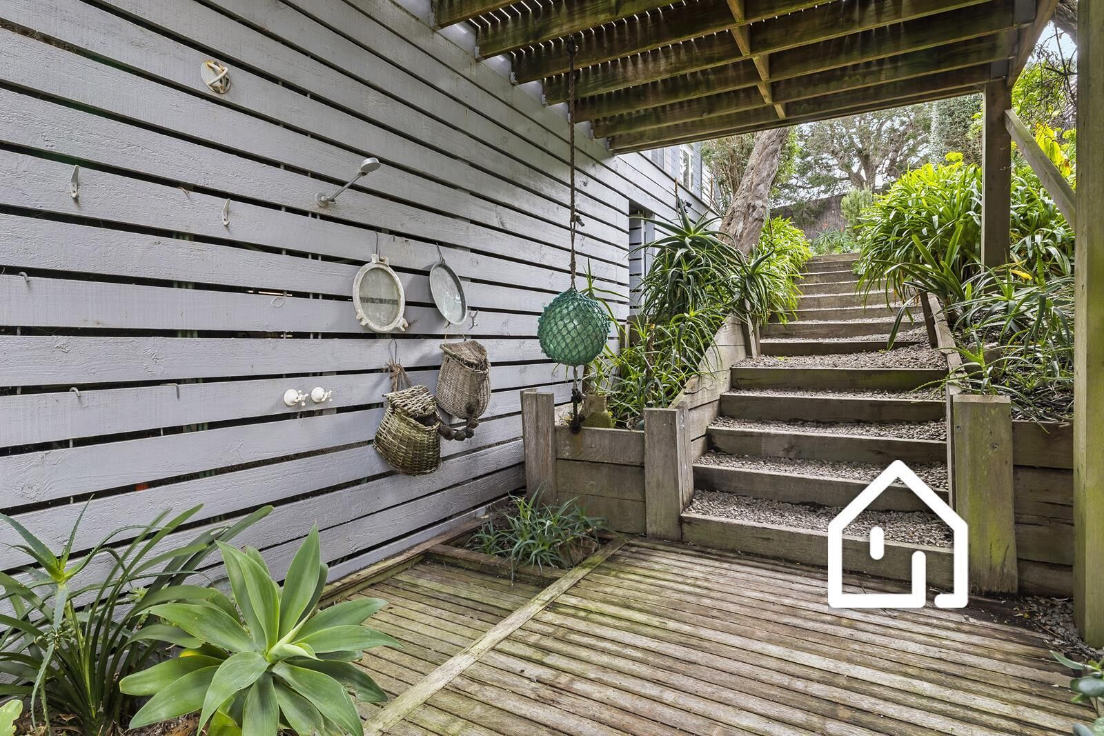 A wooden staircase leading to a house with a white exterior, surrounded by greenery and a small garden area.