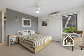 A bedroom with a bed, bedside tables, a ceiling fan, wall art, an air conditioning unit, and a window with a view of greenery. - Ocean Whispers *1 NIGHT FREE* Blairgowrie Back Beach Retreat (Blairgowrie)
