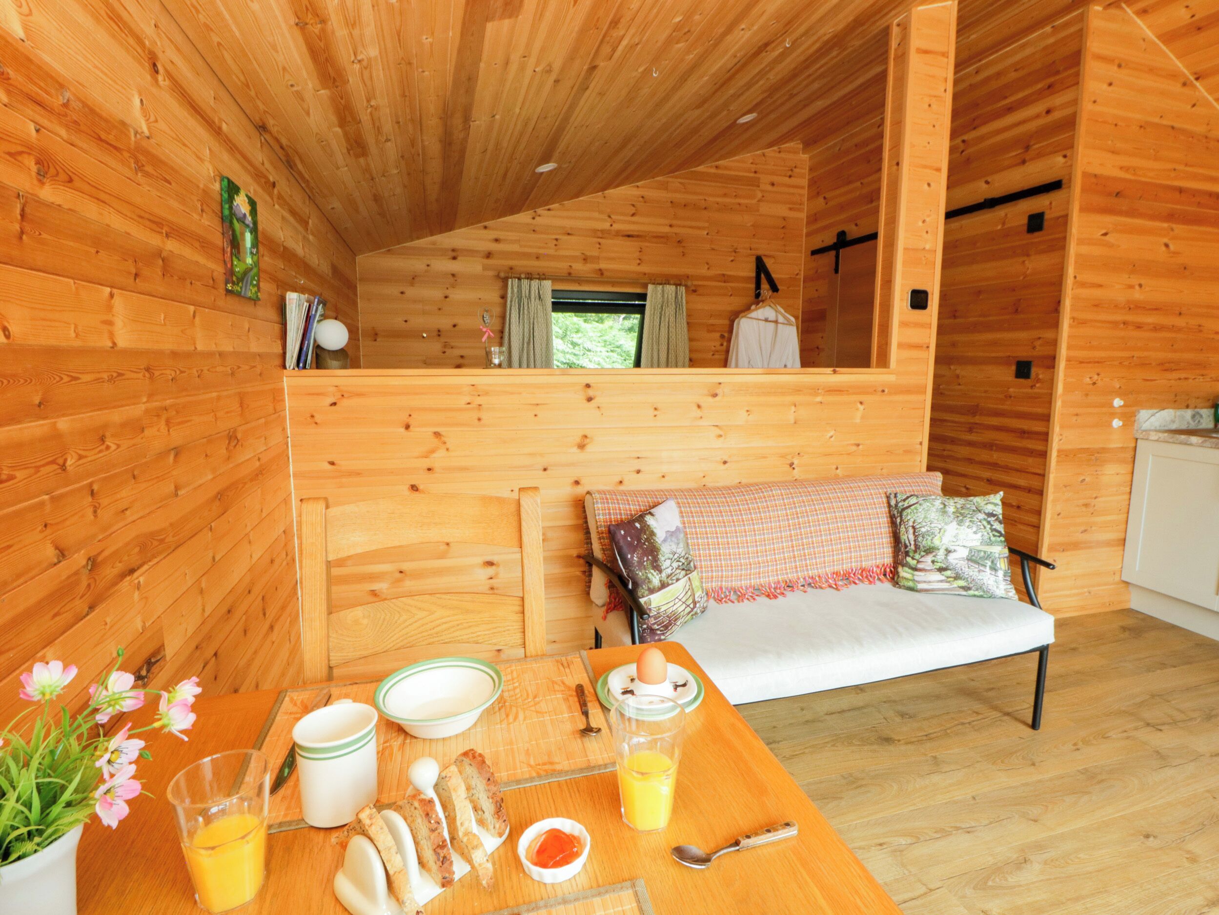 Ein Interieur einer Holzhütte mit Esstisch, gedecktem Frühstück, einer Couch mit Kissen und einem Fenster mit Vorhängen.