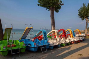 A row of colorful paddle boats lined up on a sandy beach with the sea in the background. - Mobile home with air conditioning and parking (Sirmione)