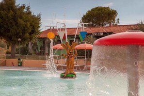 A water feature with a tree-like sculpture in a pool area, surrounded by lounge chairs and a building with a red-tiled roof. - Mobile home with air conditioning and parking (Sirmione)