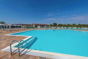 A swimming pool with a diving board, lounge chairs, and a building in the background. - Mobile home with air conditioning and parking (Sirmione)