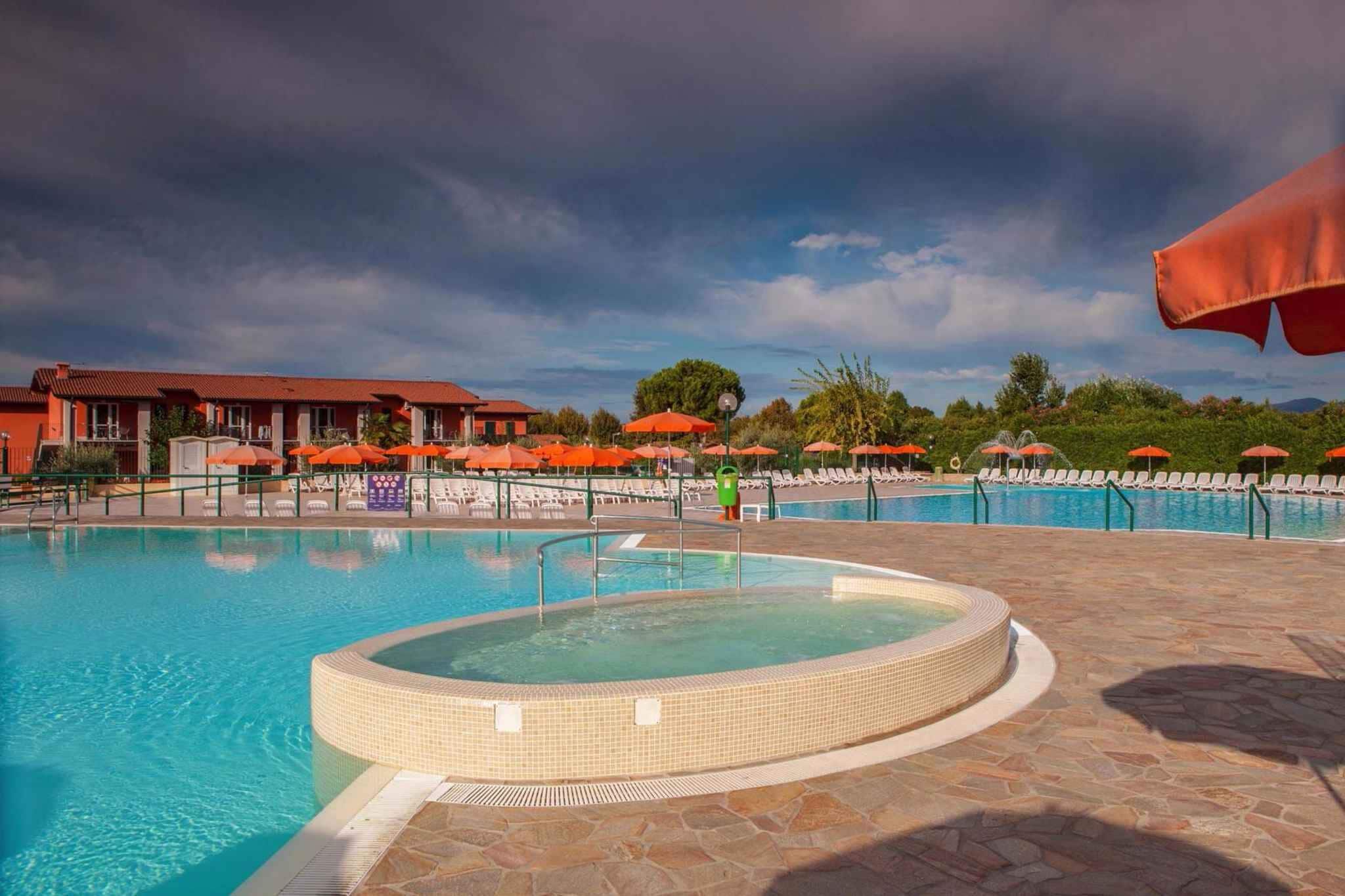 Une piscine avec un jacuzzi, des chaises longues et des parasols.