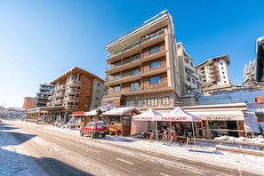 A multi-story building with balconies, a ski service tent, and a red vehicle parked in front. - Appartamento Venus 11, Sestriere, Italy (Sestriere)