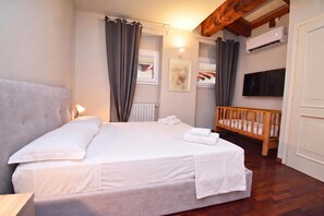 A bedroom with a bed, a wooden crib, a radiator, a TV, and a window with curtains. - Luke Loft Lakeside Charm Central park, Salò, Italy (Salò)