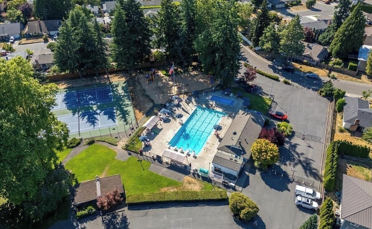 An aerial view of a residential area with a swimming pool, tennis courts, and a parking lot.