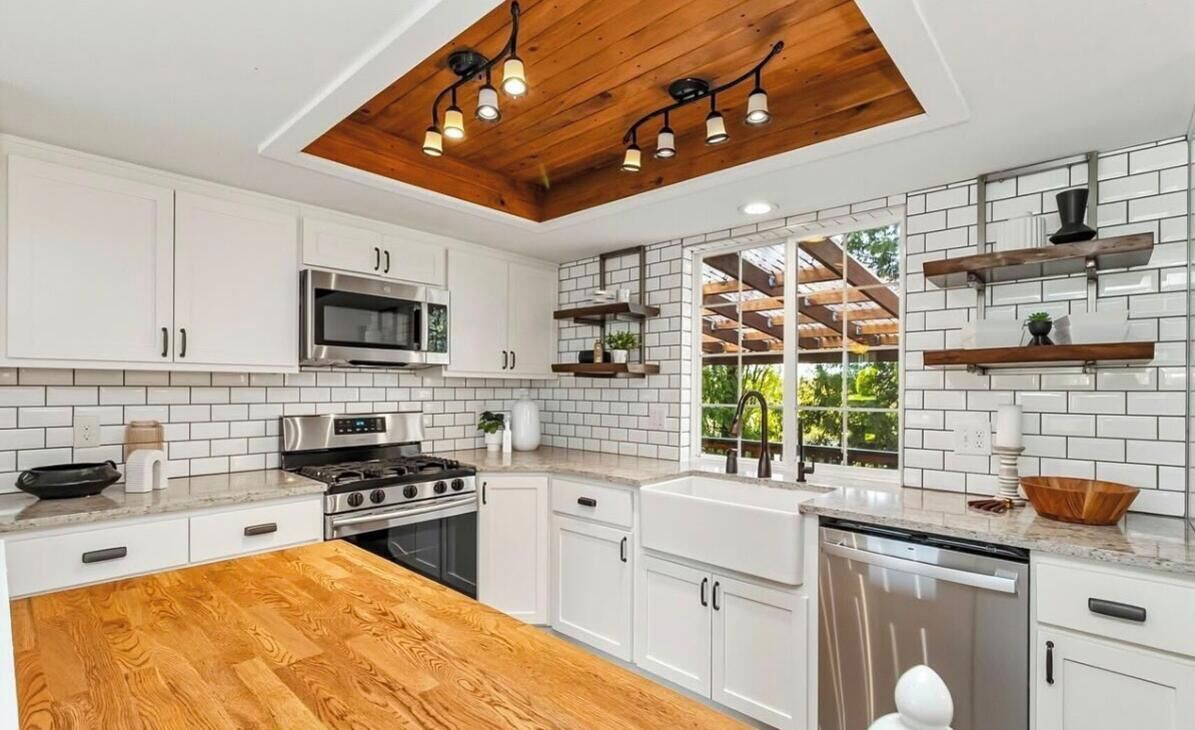Una cocina moderna con armarios blancos, piso de madera y un respuesto de ladrillo.