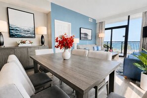 A modern living room with a dining area, a balcony with a view, and a blue accent wall. - Fully Renovated Direct Oceanfront Corner Unit Perfect for Family Gateway (Myrtle Beach)