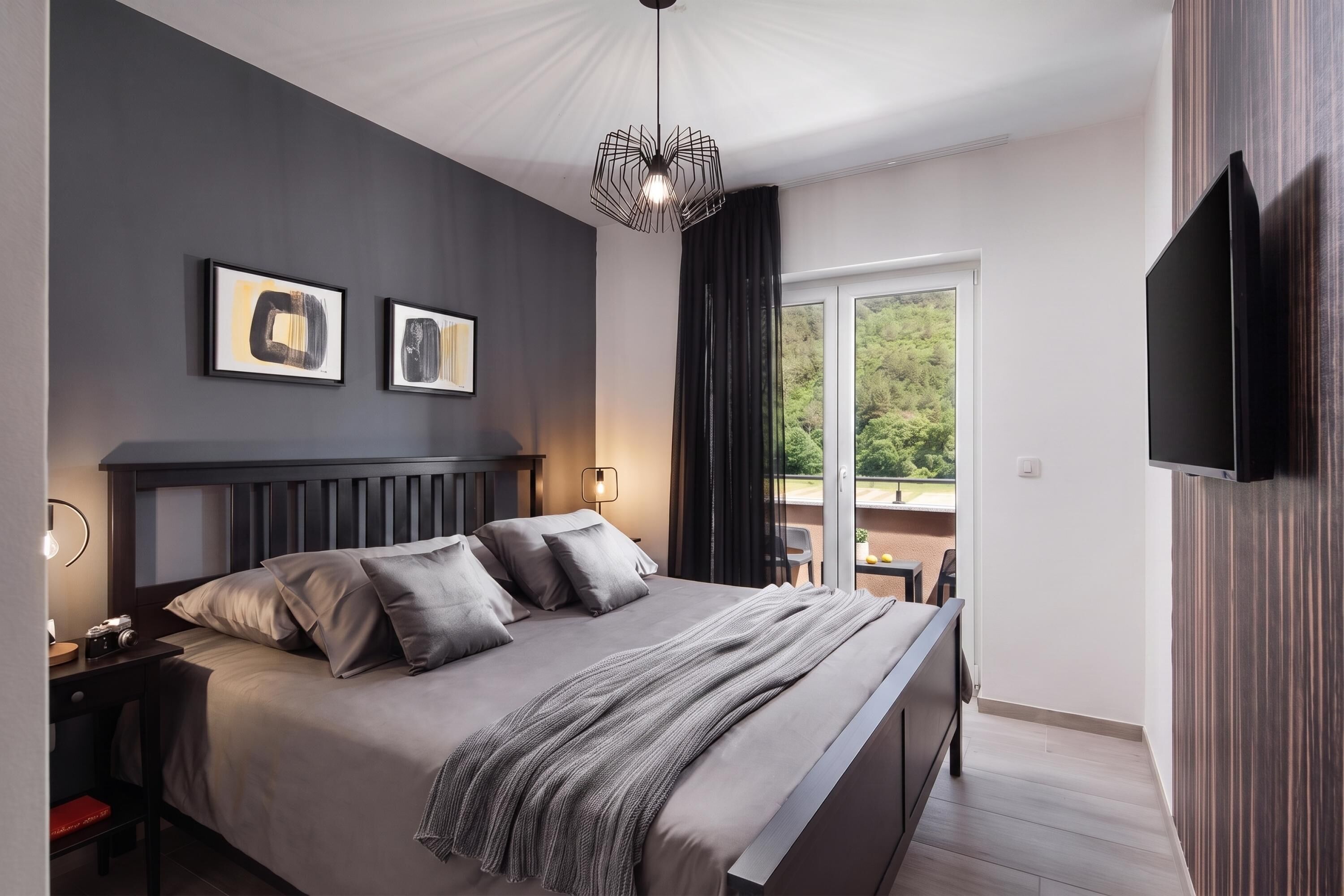 A modern bedroom with a bed, bedside tables, a flat-screen TV, and artwork on the wall.