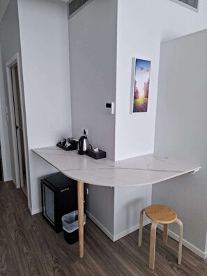 Habitación compacta con encimera de mármol blanco, un taburete pequeño, un cesto de basura y un cuadro en la pared.