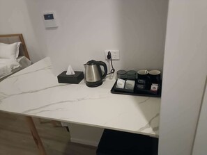 Habitación de hotel con encimera de mármol, tetera, caja de pañuelos y bandeja con bolsitas de té y tazas.