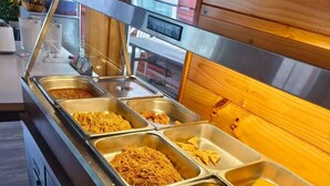 Un bufé con diversos alimentos en bandejas metálicas.