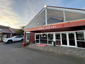 A hotel with a large glass facade, a red awning, and a white car parked in front.