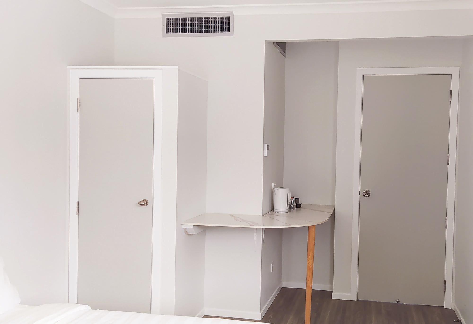 Una habitación con una cama, una mesita con una taza y dos puertas.