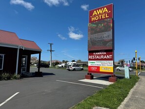 Señal de hotel que indica 'AWA HOTEL' y 'KAWAHA RESTAURANT', un estacionamiento y un edificio con techo rojo.