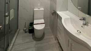 Un baño moderno con cabina de ducha de vidrio, inodoro y un lavamanos grande con espejo.