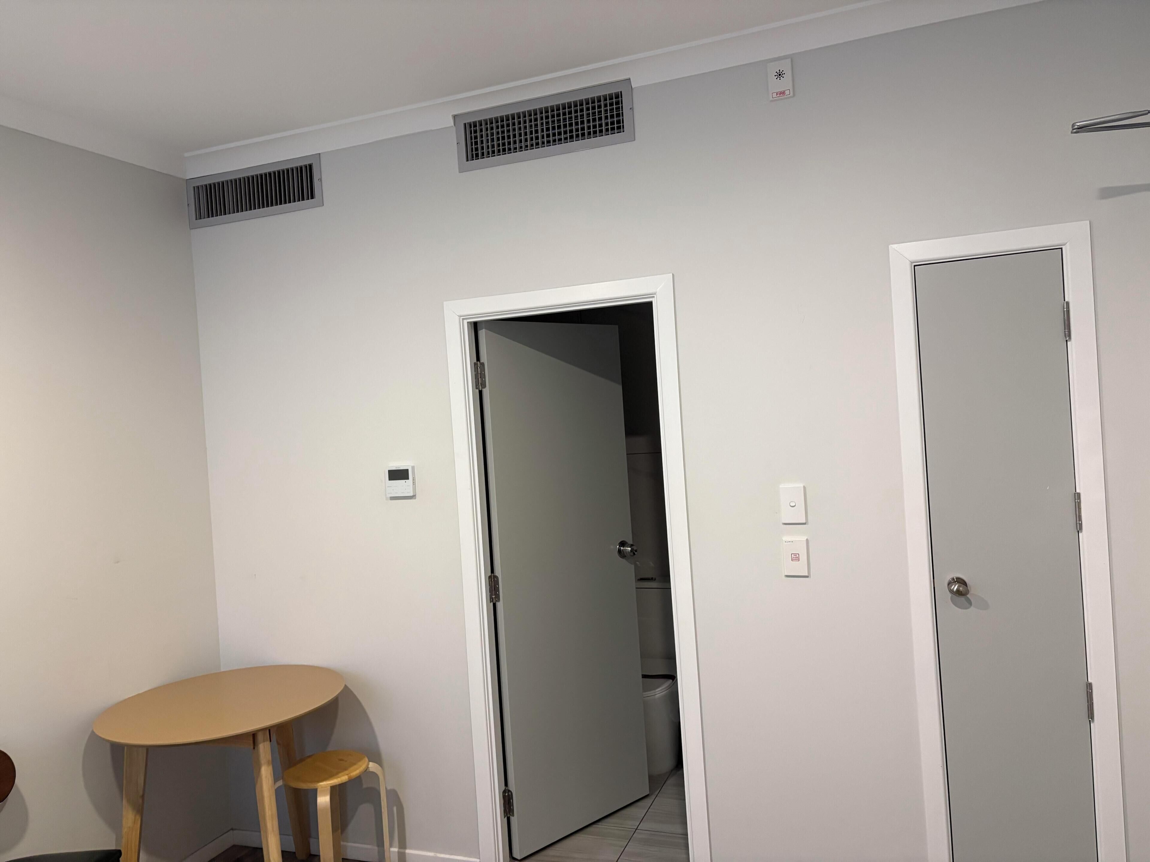 A room with a door, a table with a chair, and a toilet visible through the door.